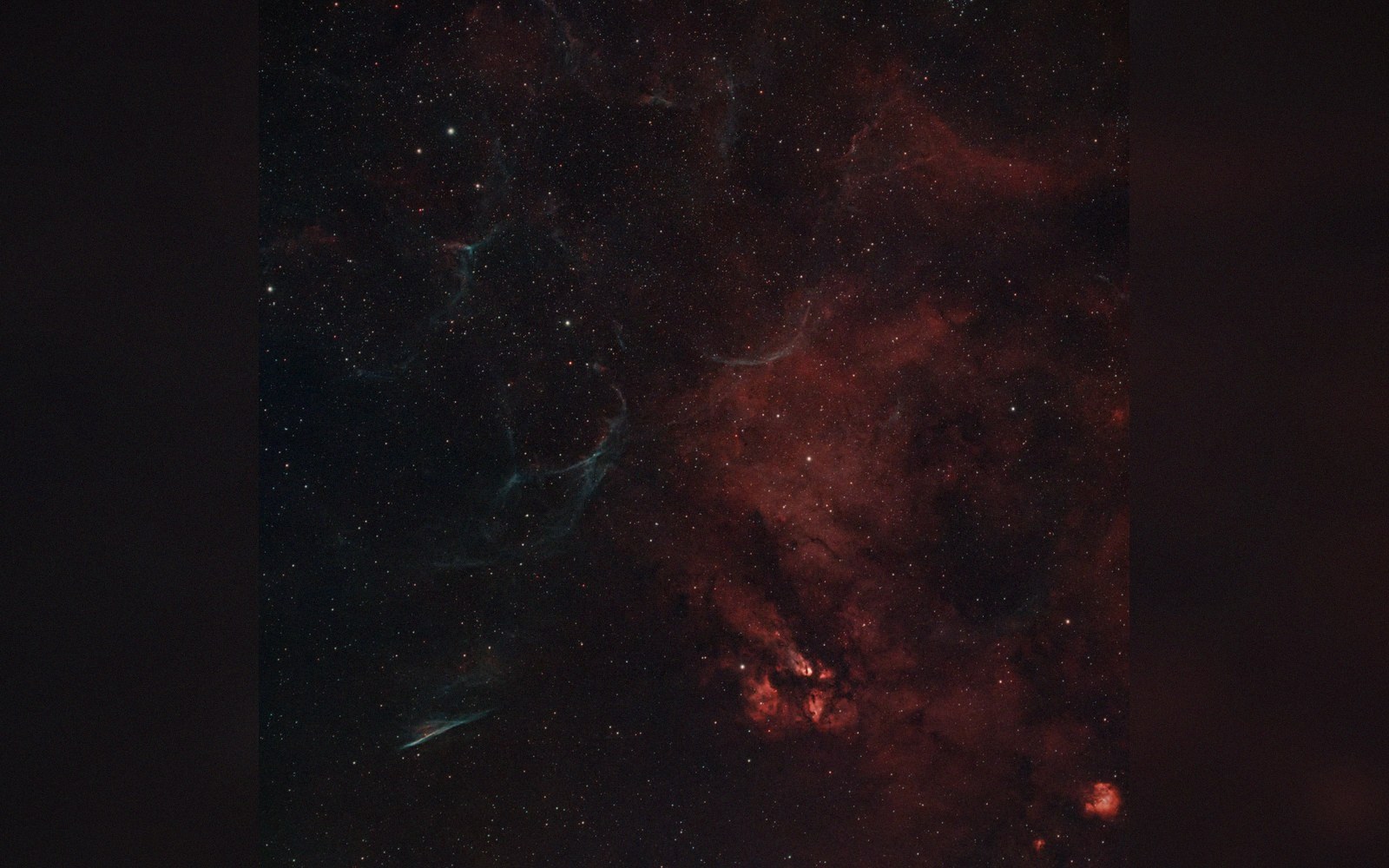 Wispy blue filaments and reddish dust clouds stretch across a dense star field