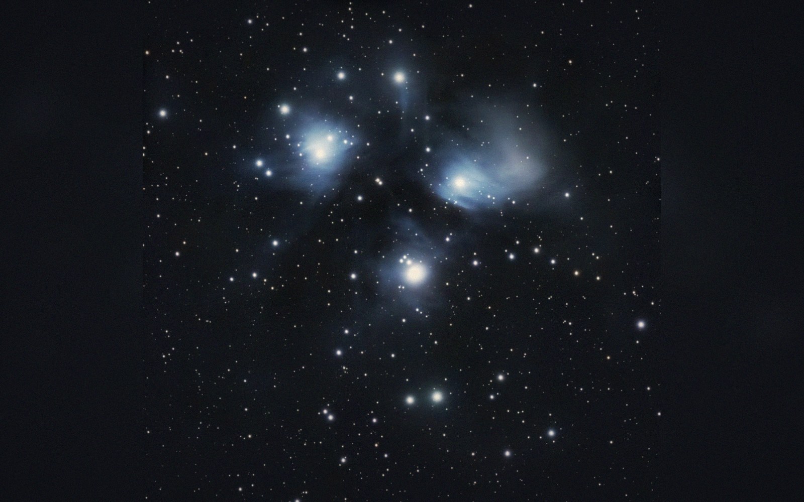 Bright star cluster wrapped in wispy blue reflection nebulosity against a dense starfield